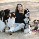 Happy woman sitting outdoors with a group of seven dogs on a sunny day.
